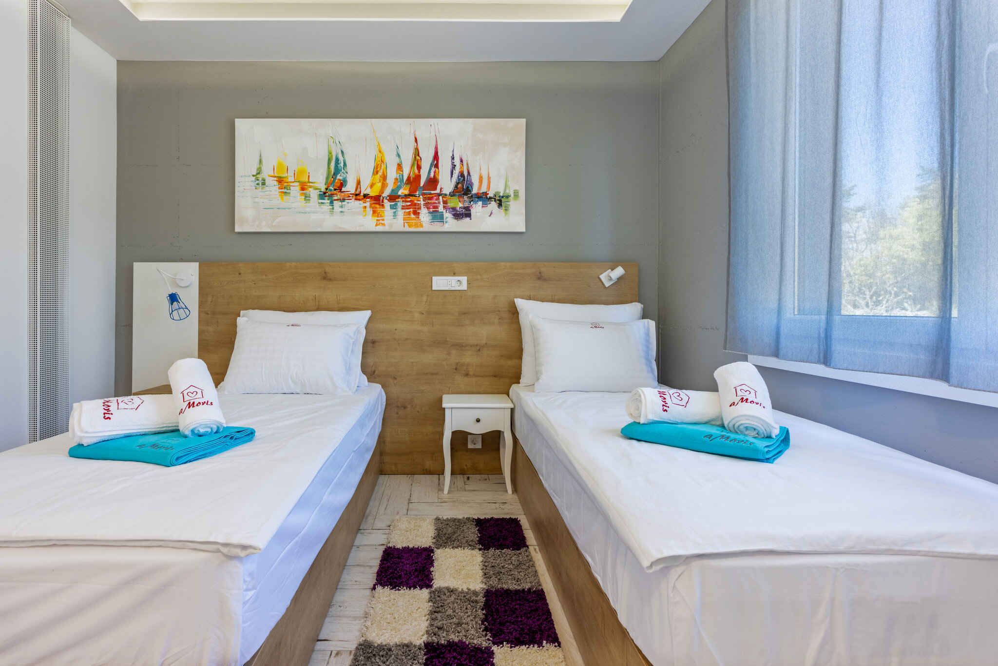 Ein Hotelzimmer mit zwei Betten, einem hölzernen Kopfteil, einem karierten Teppich und einem Bild von Segelbooten.