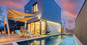 Una casa moderna con piscina, mobiliario exterior y un muro de piedra.