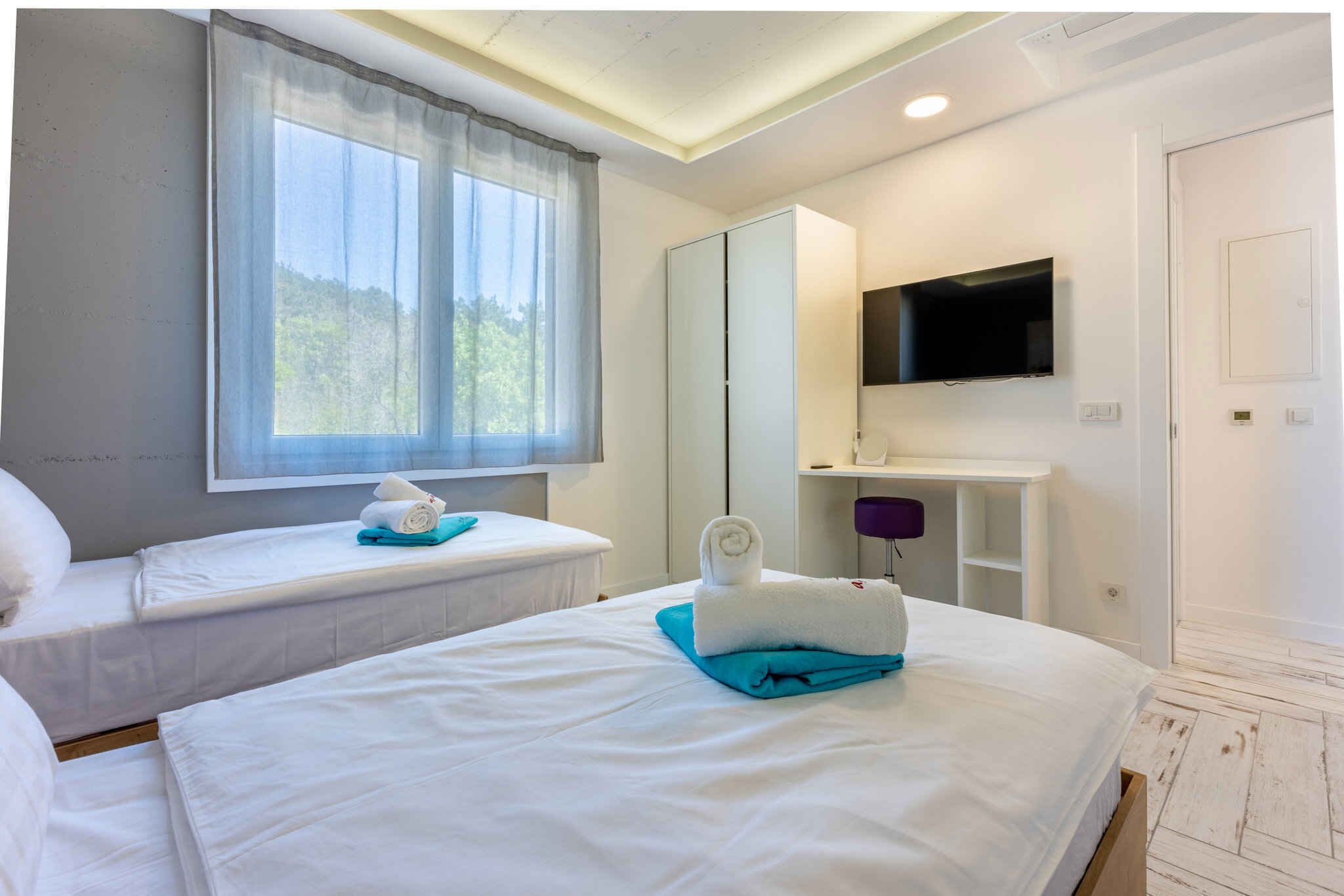 A hotel room with two beds, a TV mounted on the wall, and a window with curtains.