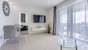 A modern living room with a flat-screen TV, a glass coffee table, and a dining area with a grey chair. - Holiday home with sea view, whirlpool and sauna (Crikvenica)