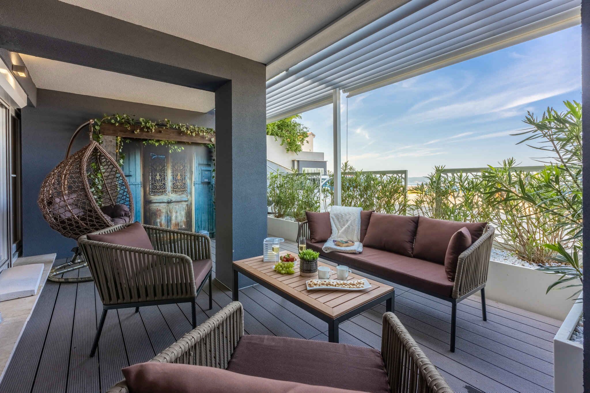 Ein Balkon mit Korbmöbeln, einem Hängestuhl und einer Couch.
