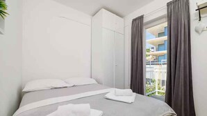 Un dormitorio con cama, armario, vista al balcón y ventana con cortinas.