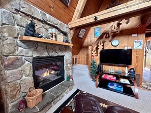 A cozy living room with a stone fireplace, a television on a wooden stand, and a small Christmas tree. - U.P Norse A-frame ~ Your Adventure Basecamp! (Bessemer)