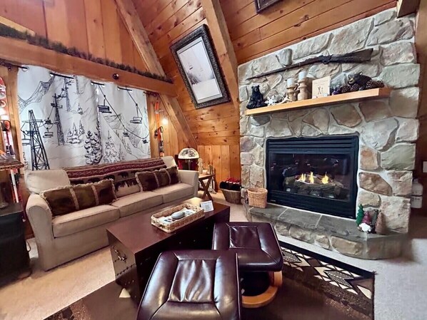 A cozy living room with a stone fireplace, a sofa, a coffee table, and a fireplace screen.