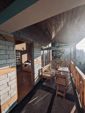 Enjoy a peaceful retreat with a scenic view of trees and mountains from this balcony, featuring a seating area with a bench and chairs.