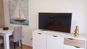 Ein Essbereich mit einem weißen Tisch, zwei Stühlen, einer Schüssel, einem Bild eines Segelbootes und einem Fernseher auf einem weißen Schrank.