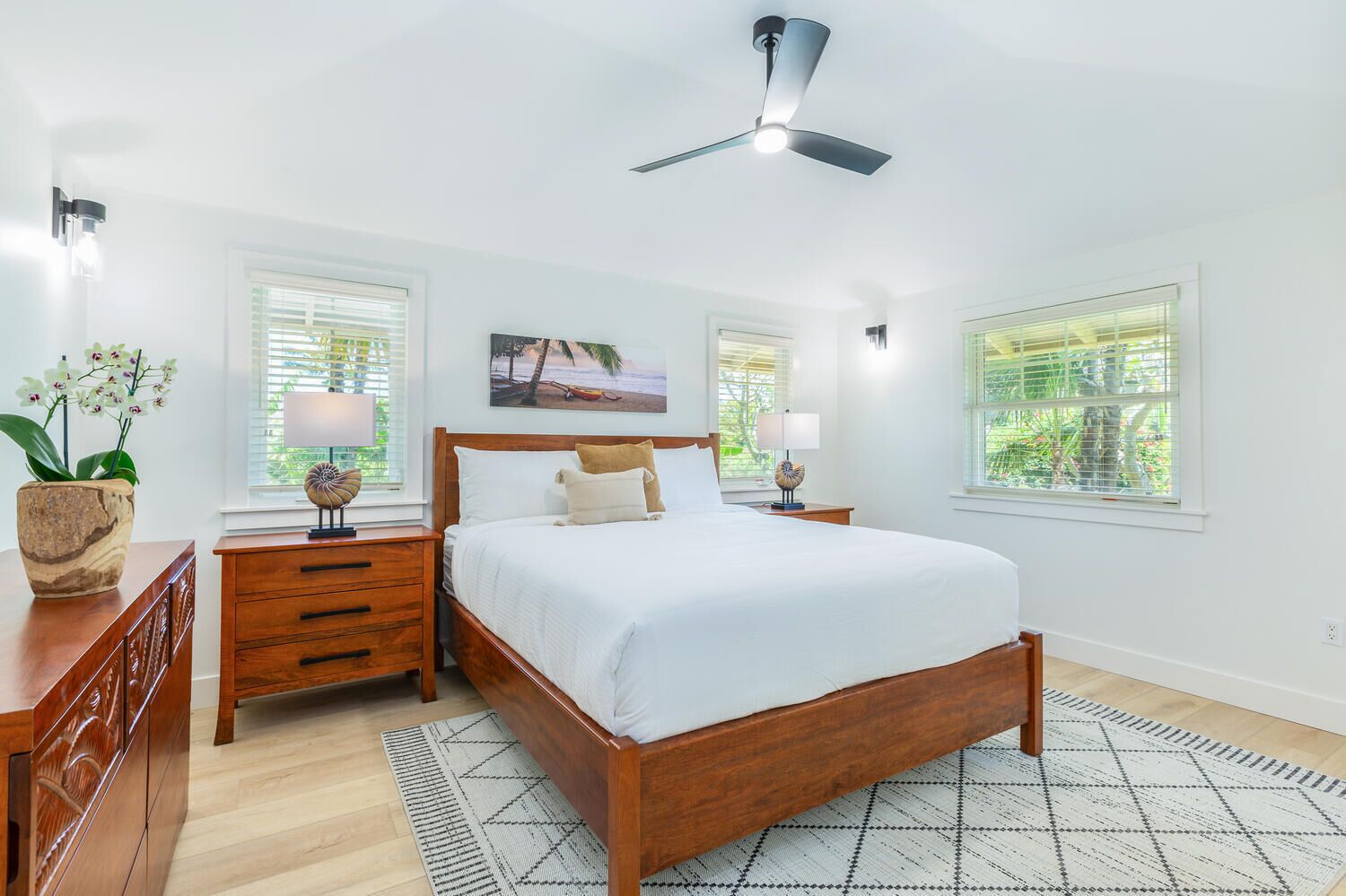 A bedroom with a wooden bed, nightstands, a ceiling fan, and large windows with blinds.