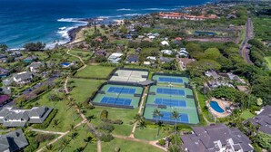 Vista aerea di una zona residenziale costiera con diverse piste da tennis, case e una spiaggia.