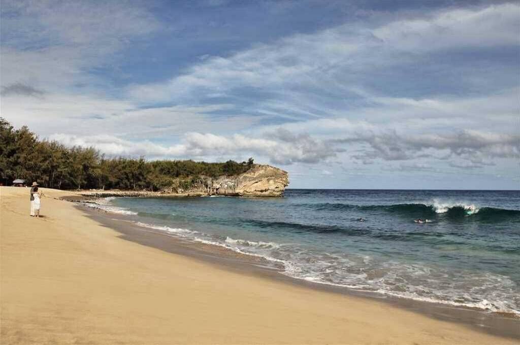 A beach with a rocky outcrop, calm sea, and a person in a white dress.