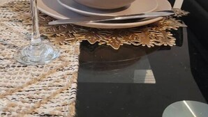 Una mesa de comedor dispuesta con platos, tazones y una copa de vino, con un jarrón de flores secas a la izquierda.
