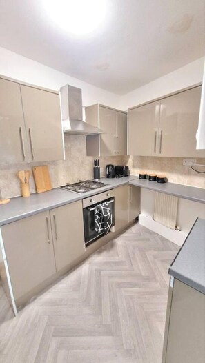 A modern kitchen with a herringbone wood floor, stainless steel appliances, and light-colored cabinetry. - 4-bed House in Accrington (Accrington)
