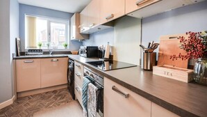 Una cucina moderna con mobili chiari in legno, un piano cottura nero e un tagliere di legno con la scritta 'TEA'.