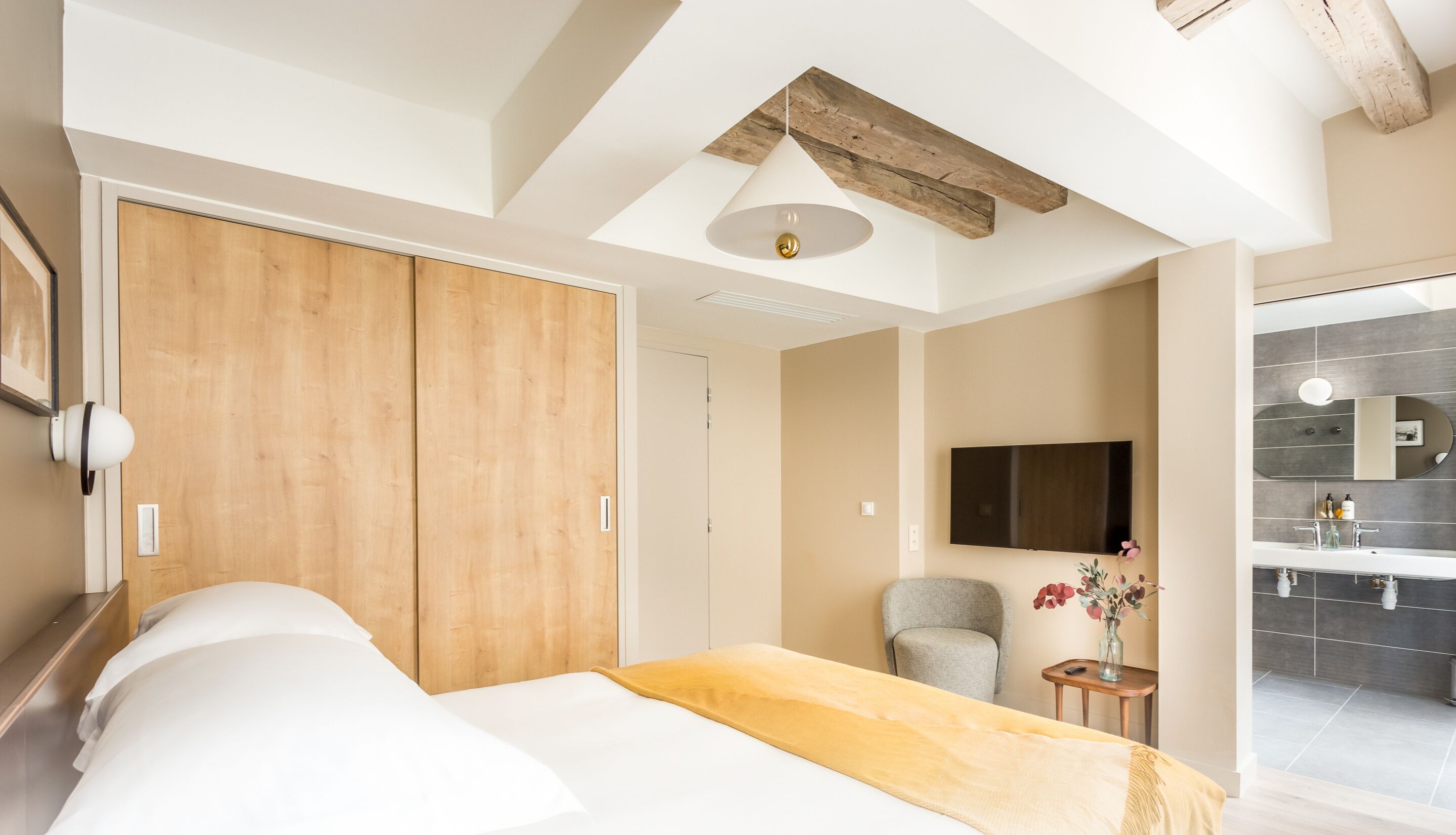Un dormitorio moderno con una cama grande, un armario de madera y un televisor montado en la pared.