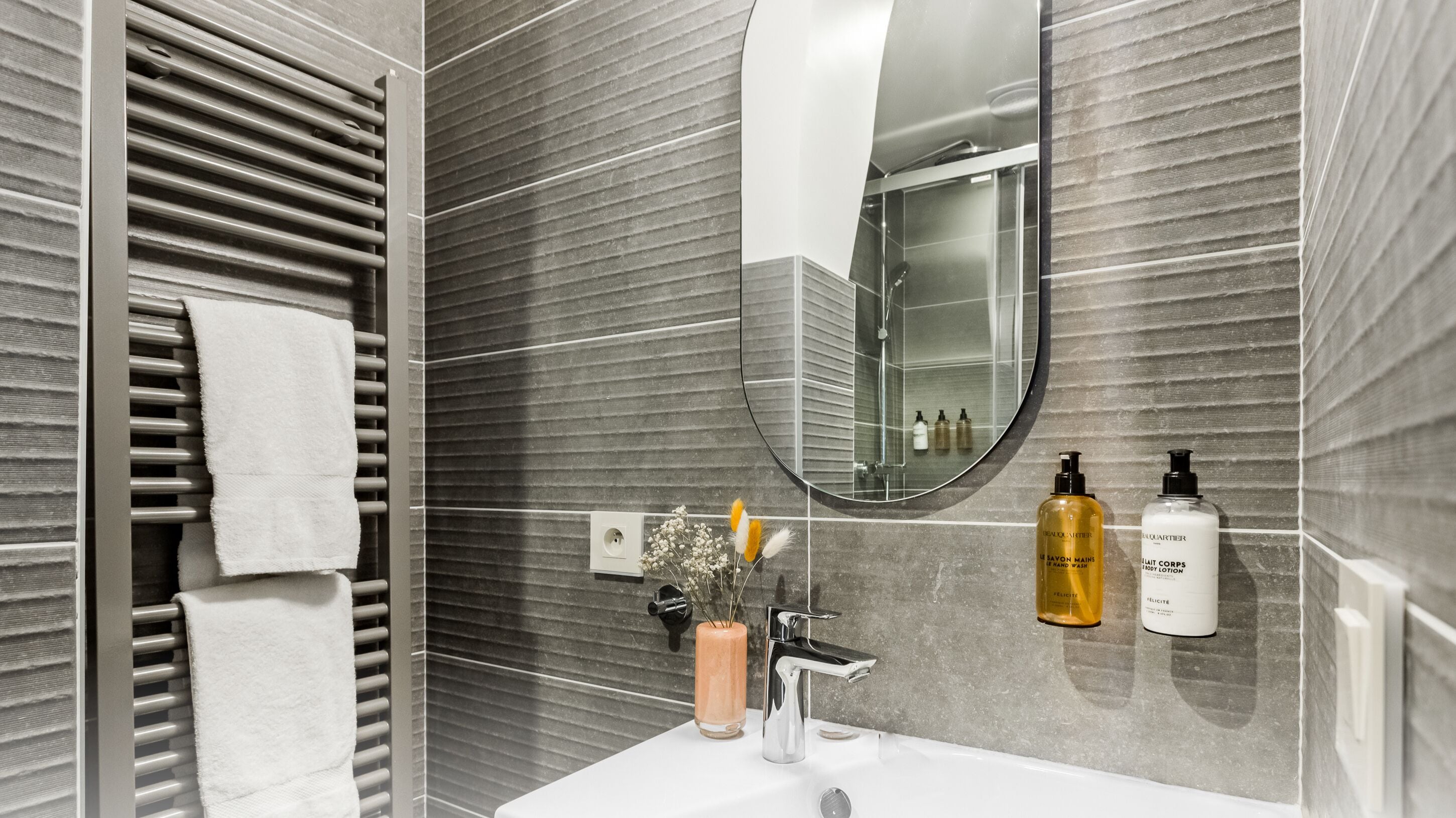 Ein modernes Badezimmer mit Handtuchhalter, Spiegel, Waschbecken und Pflegeprodukten.