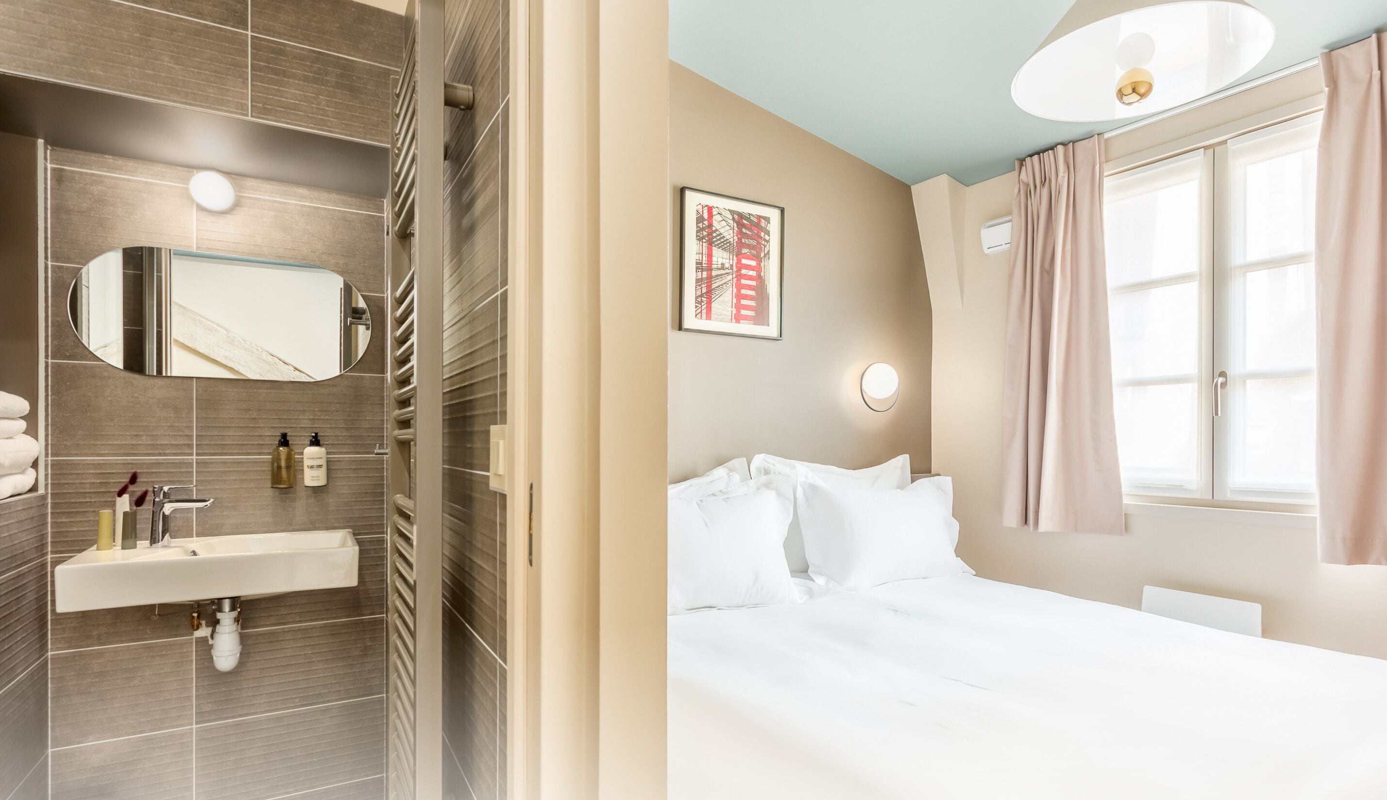 A modern bathroom with a sink, mirror, and towel rack, and a bedroom with a bed, window, and artwork.