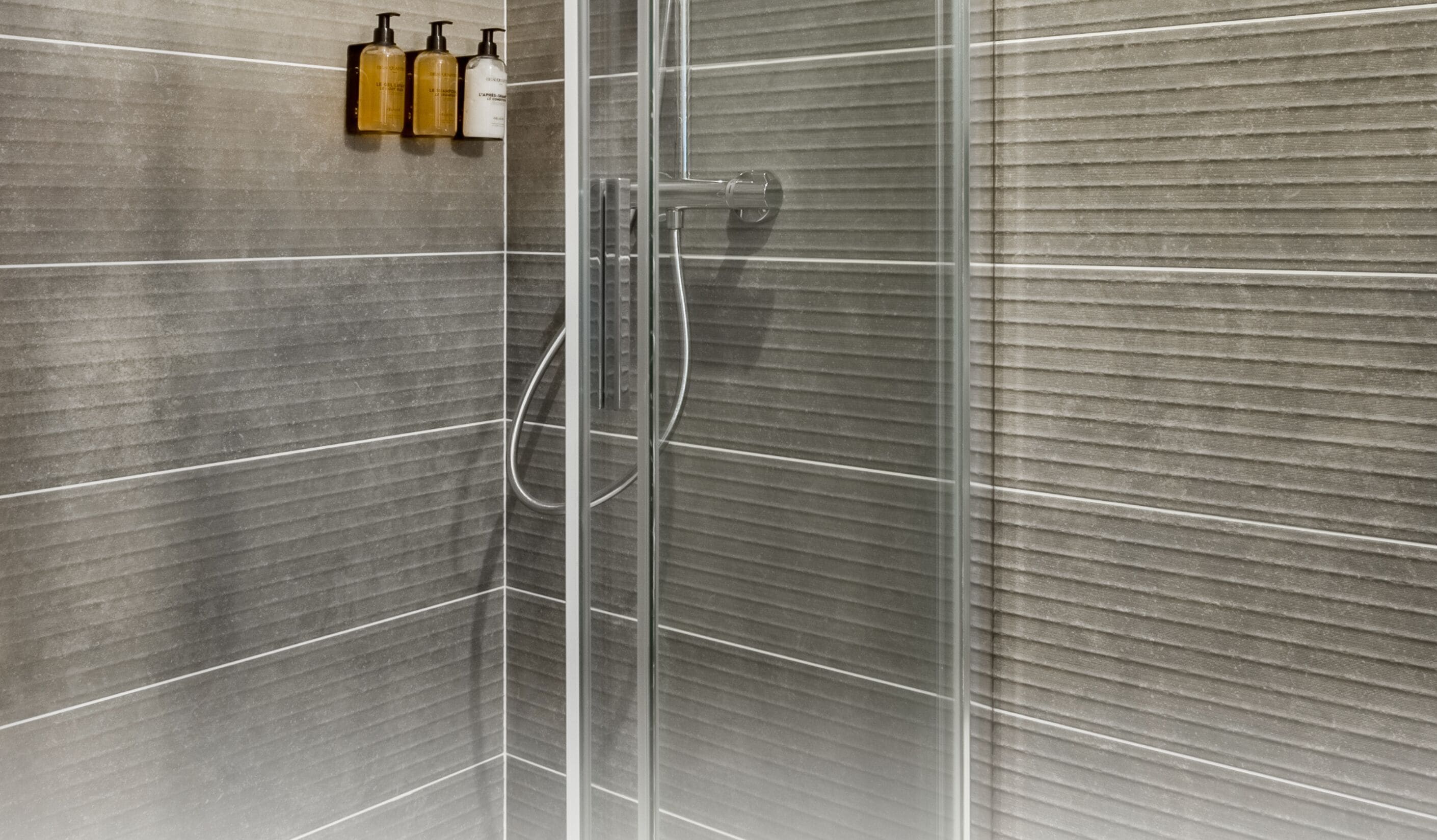 A modern shower with clear glass doors, a handheld showerhead, and a wall-mounted soap dispenser.