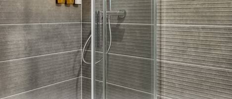 A modern shower with clear glass doors, a handheld showerhead, and a wall-mounted soap dispenser.