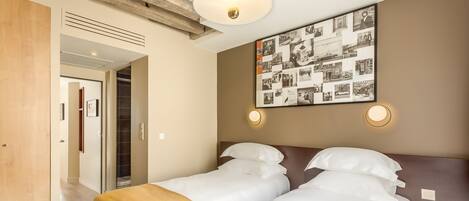 A hotel room with two beds, a wooden ceiling, a wall-mounted photo collage, and a door leading to another room.