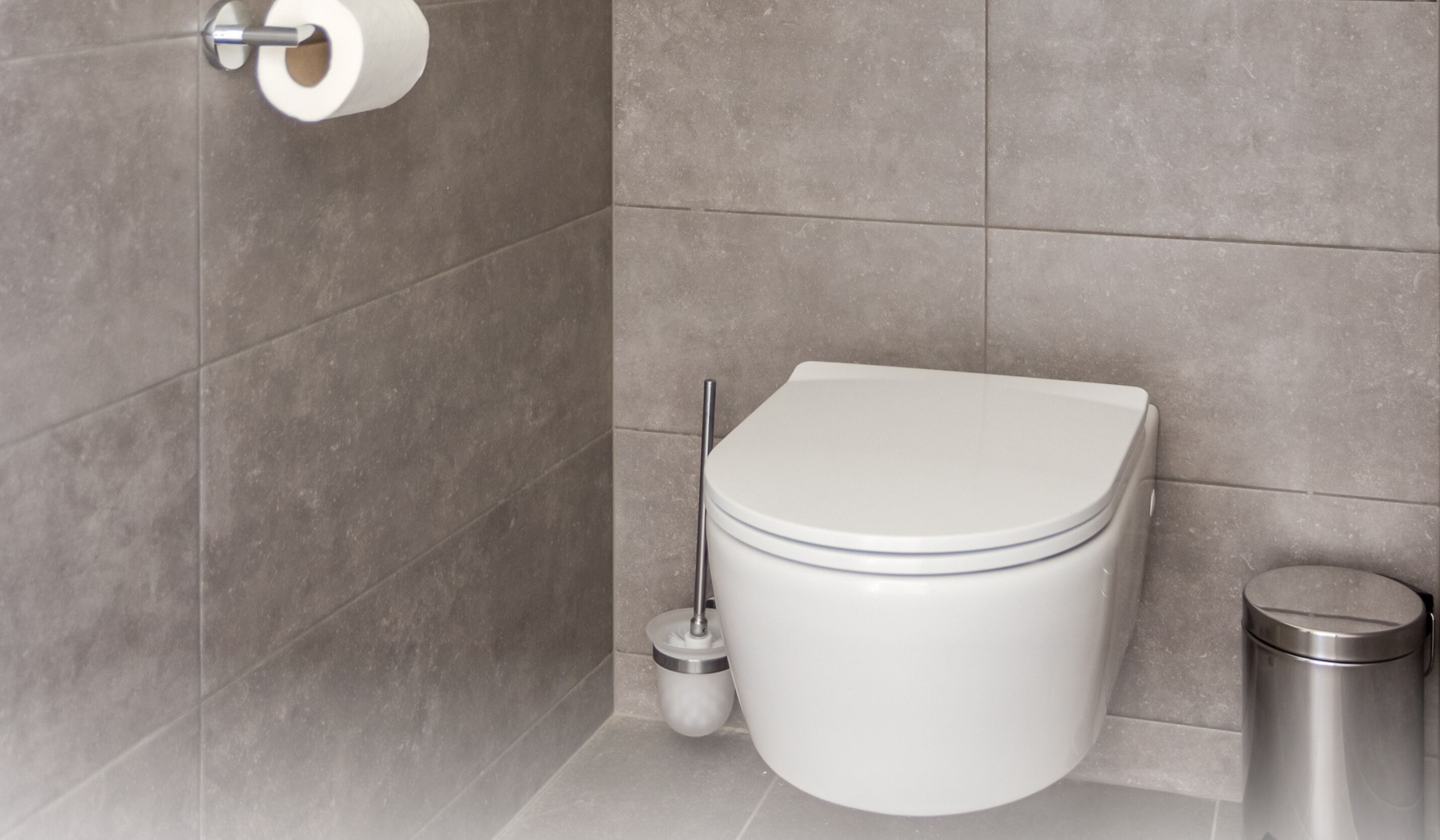 A modern bathroom with a toilet, a toilet brush, and a trash can.