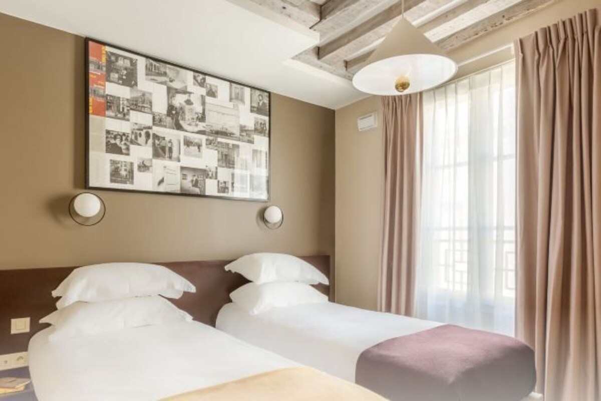 A hotel room with two beds, a large photo collage on the wall, and a window with curtains.