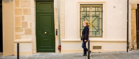 A building with a green door, a window with bars, and a person walking by.