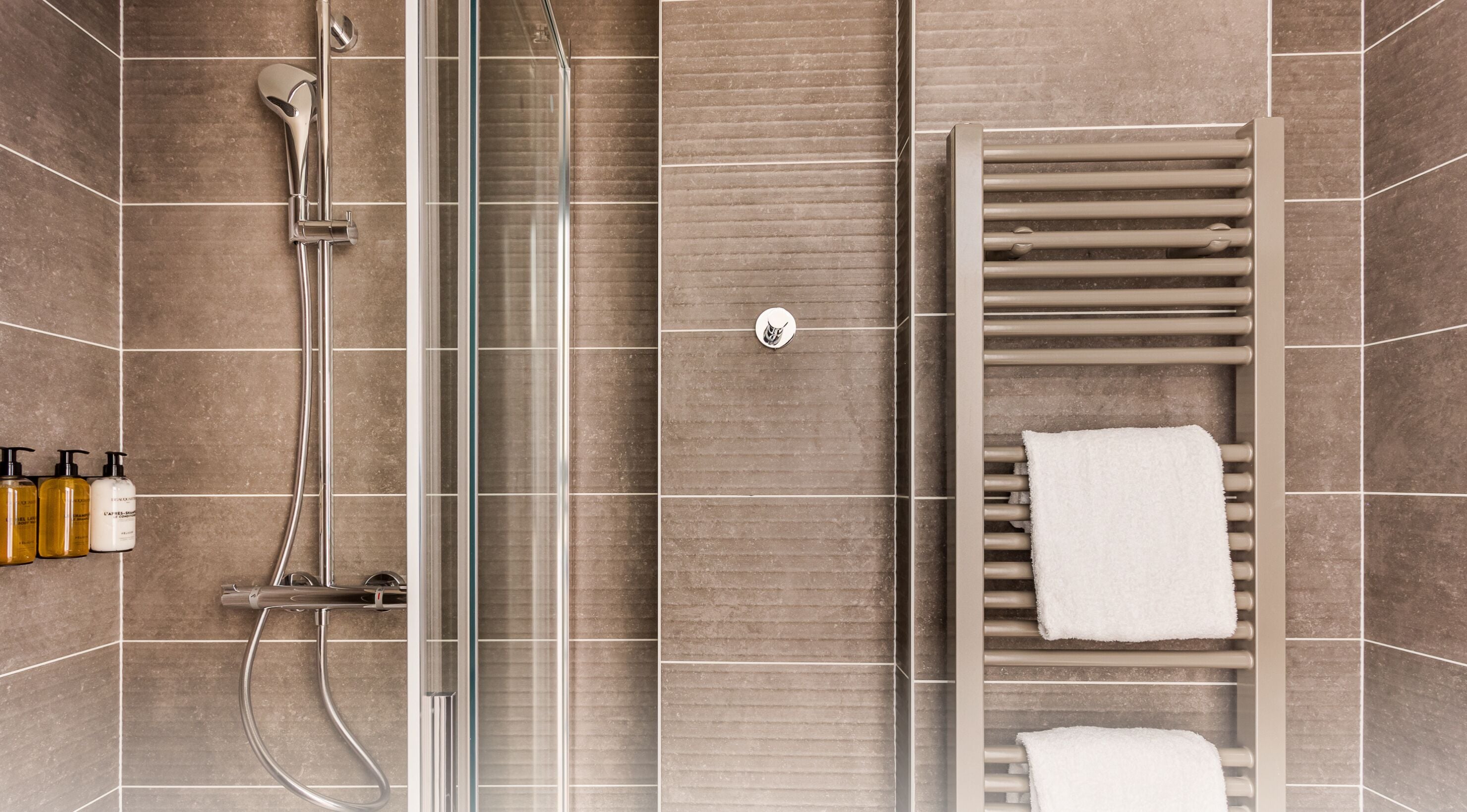 A modern bathroom with a glass shower enclosure, a built-in towel rack, and toiletries on the wall.