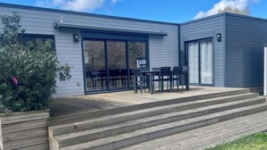 A modern house with a deck, sliding glass doors, and a small outdoor seating area. - Ecolodge 2Ch - Air conditioning - Wifi - Swimming pool and Jacuzzi open all year (Les Mathes)