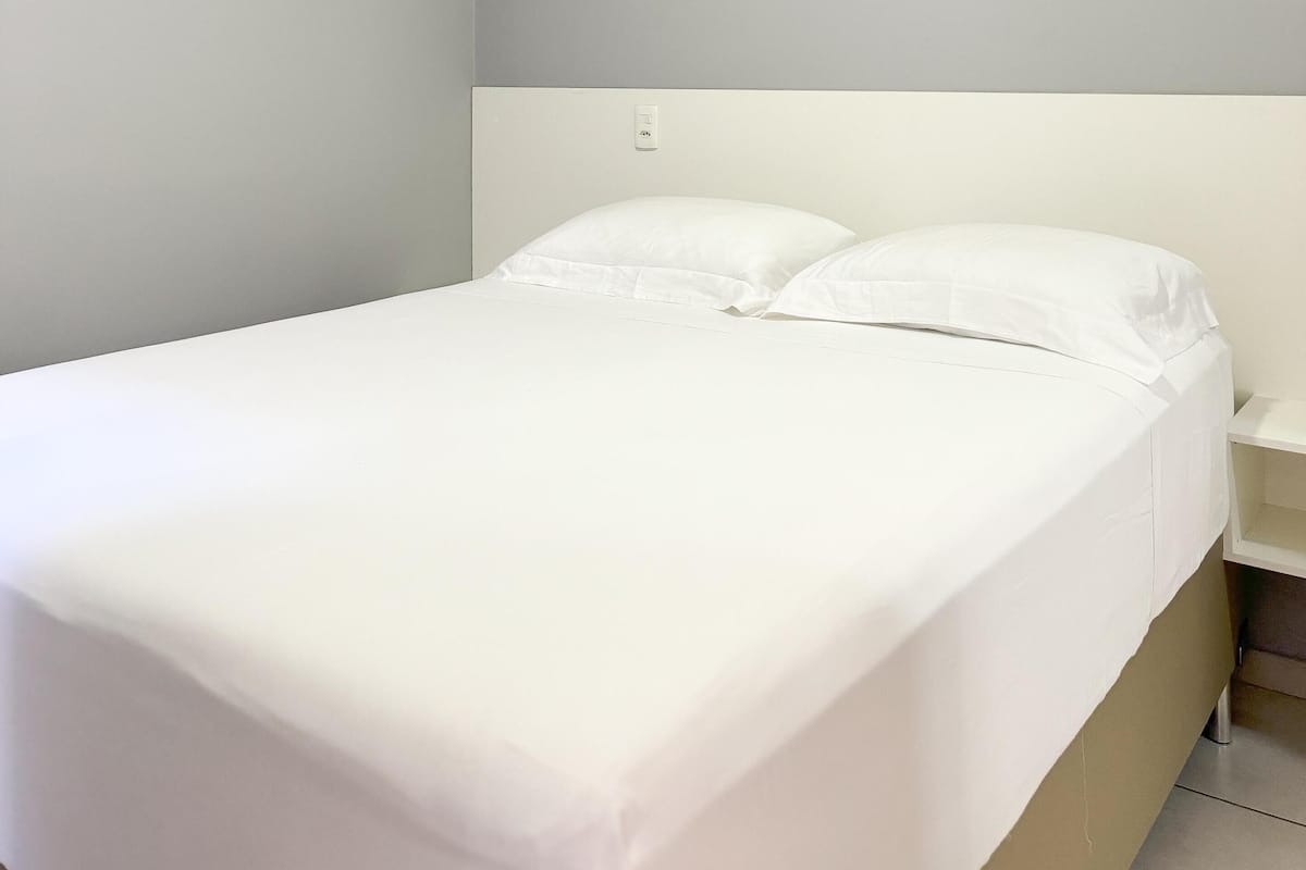 A single bed with white bedding in a room with light grey walls and a white headboard.