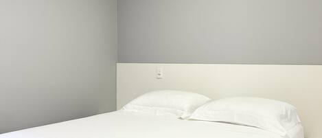A single bed with white bedding in a room with light grey walls and a white headboard.