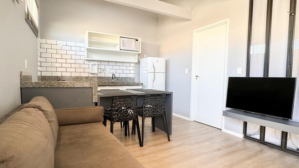 Een moderne woonkamer met een bank, een eettafel met stoelen, een keuken met een magnetron en koelkast, en een tv op een meubel.