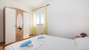Une chambre à coucher comprenant un lit, une armoire, une fenêtre avec des rideaux et une table de chevet avec une lampe.