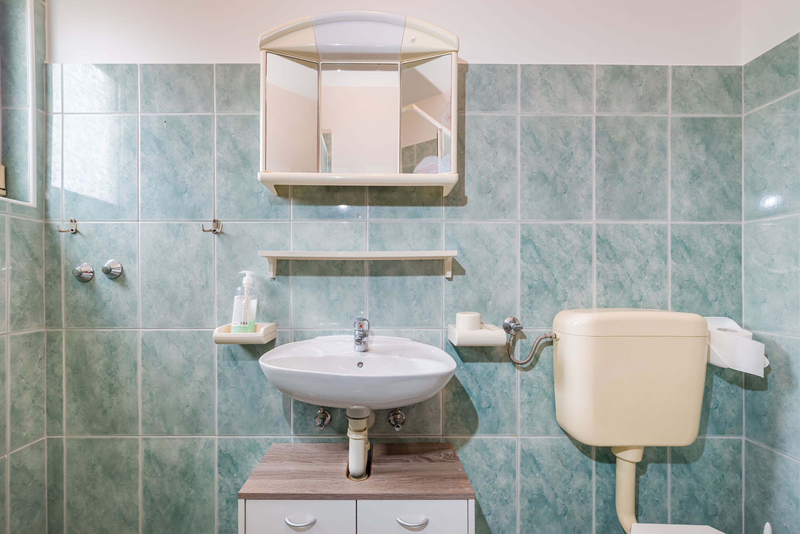 A bathroom with a sink, mirror, toilet, and storage cabinet.