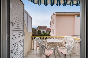 Uma varanda com mesa e cadeiras, vista de edifícios vizinhos e porta de acesso ao interior.