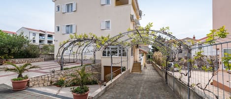 A residential building with a covered walkway, potted plants, and a metal fence.