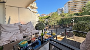 A balcony with a sofa, a table with food and drinks, and a view of buildings and greenery.