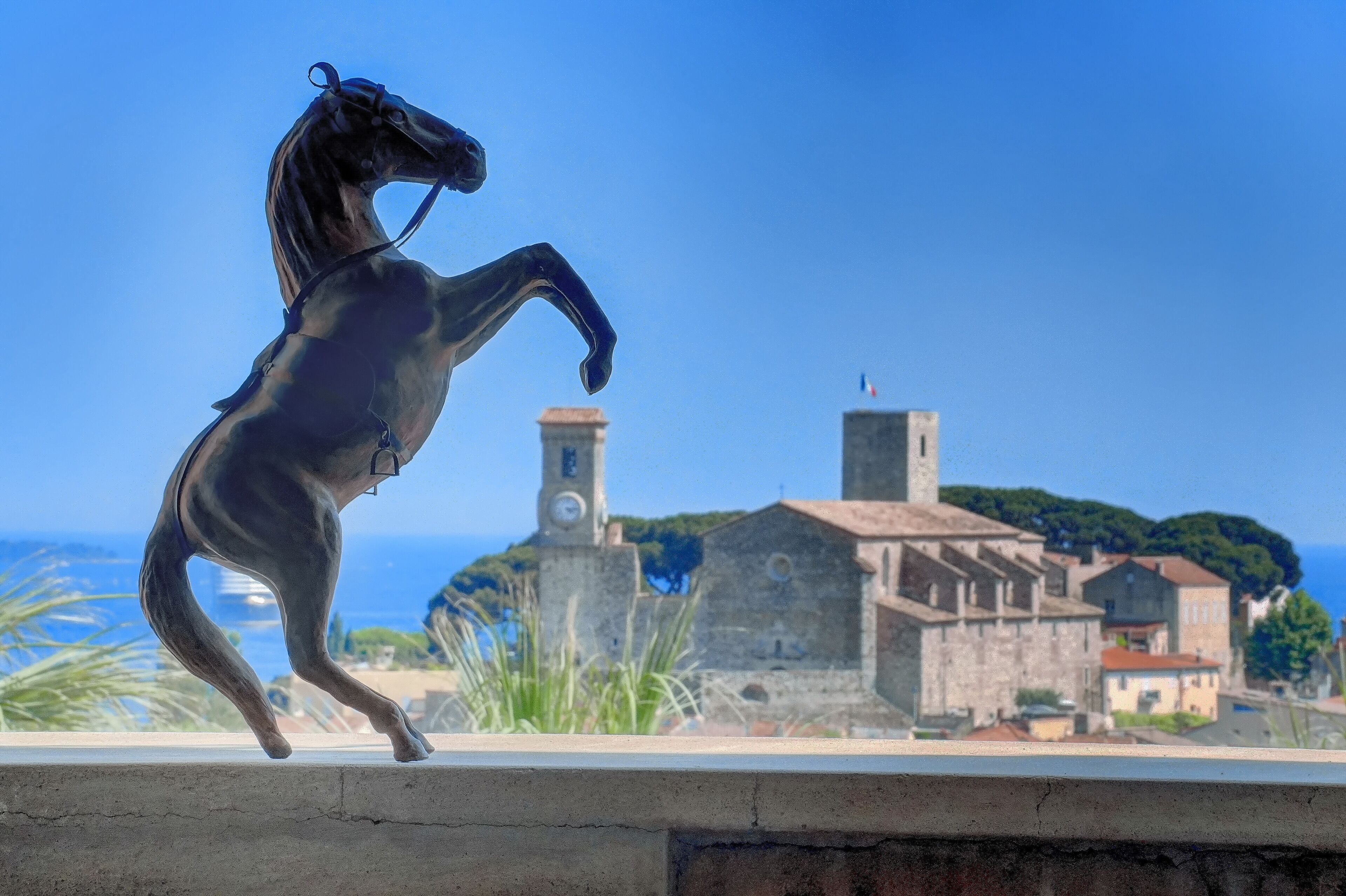 A bronze horse statue on a ledge with a coastal town and church in the background.