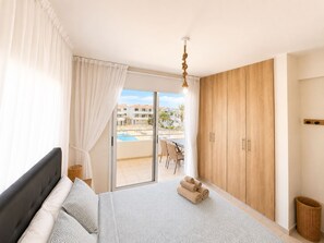 A bedroom with a bed, a wooden wardrobe, a balcony with a pool view, and a hanging light fixture.