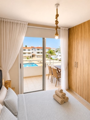 A hotel room with a bed, a view of a pool, and a dining area. - Narcissos Nissi Beach Apartment E9 (Ayia Napa)