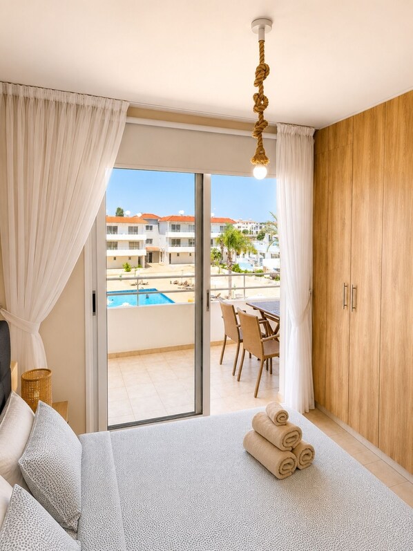 A hotel room with a bed, a view of a pool, and a dining area.