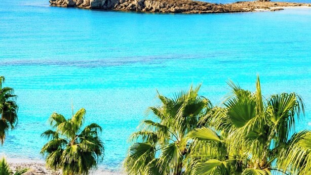 A beach with clear turquoise water, palm trees, and sun loungers. - Narcissos Nissi Beach Apartment E9 (Ayia Napa)