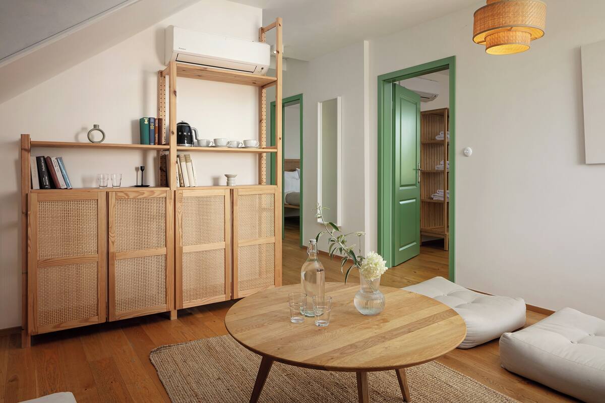 A room with a round wooden table, a wicker cabinet, and a green door.