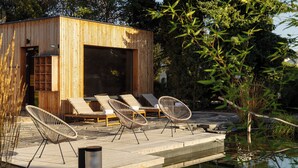 A wooden cabin with a deck, lounge chairs, and a pond. - po.spolu wellness resort (Mokrovraty)