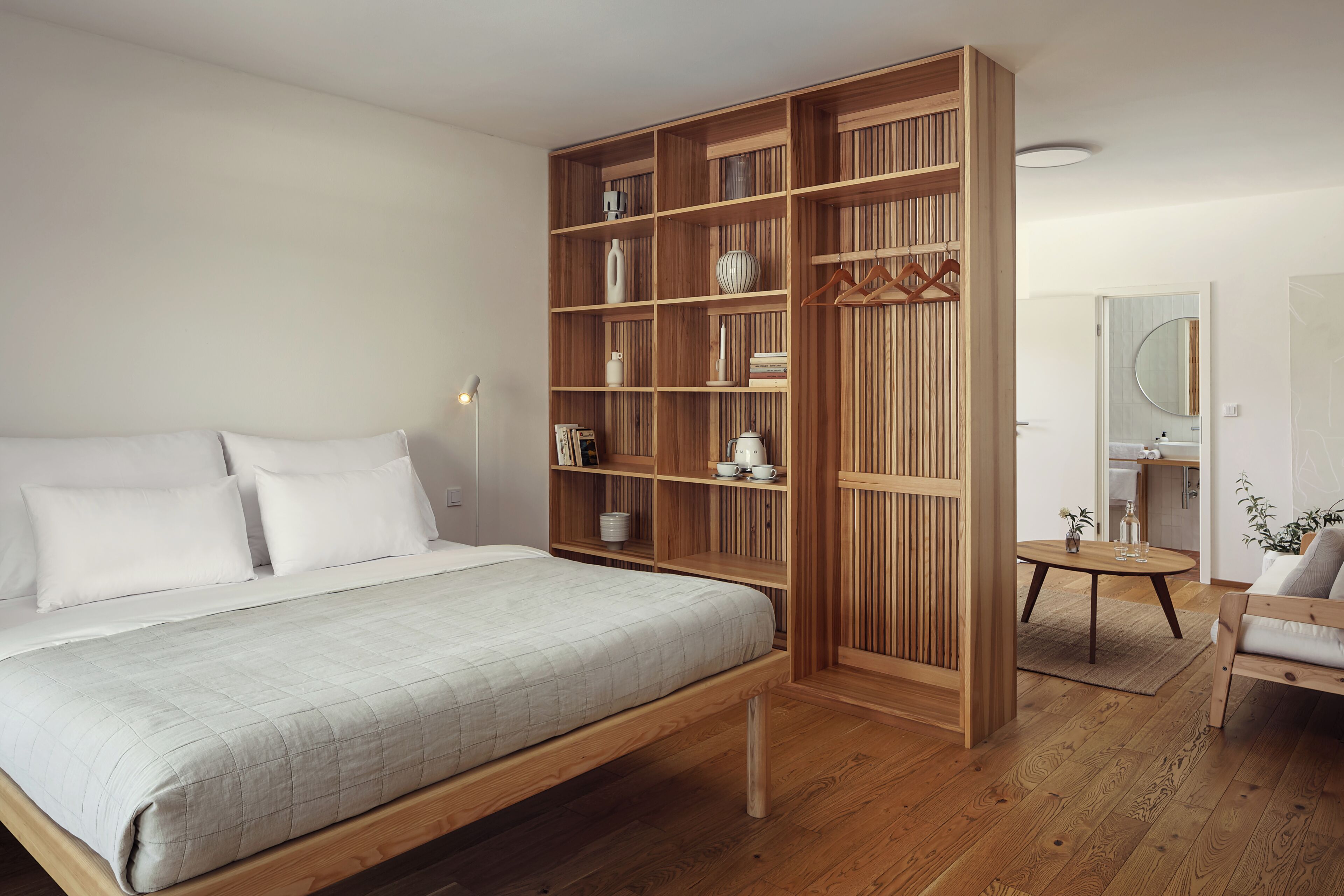 A bedroom with a bed, wooden shelving unit, and a small table with a chair.