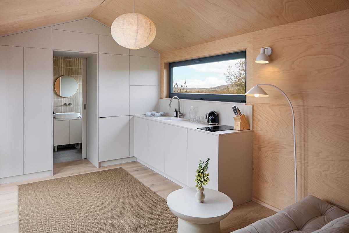 A modern kitchen with a window, white cabinets, a sink, and a round mirror.