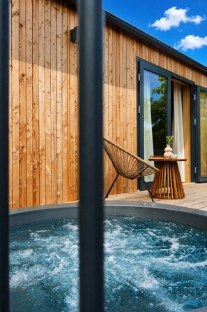 A wooden exterior wall, a glass door, a hot tub, a wicker chair, and a small table with a plant. - po.spolu wellness resort (Mokrovraty)