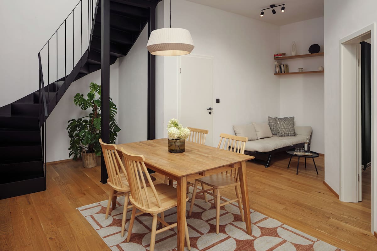 A dining area with a wooden table, chairs, a potted plant, and a staircase.