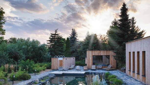 A modern outdoor pool area with a wooden deck, lounge chairs, and a wooden structure with a large window. - po.spolu wellness resort (Mokrovraty)
