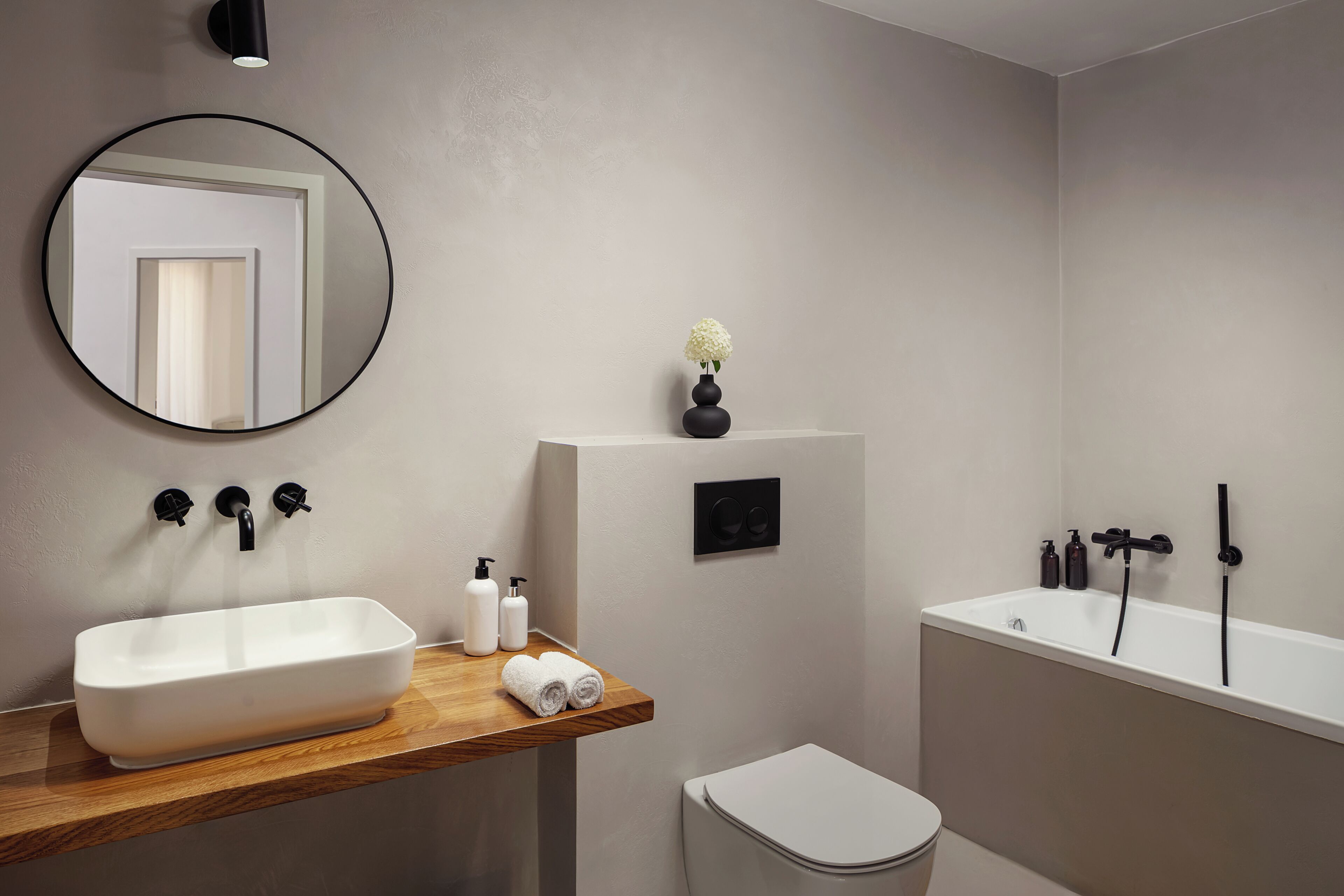 A modern bathroom with a rectangular sink, a round mirror, a toilet, and a bathtub.