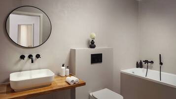 A modern bathroom with a rectangular sink, a round mirror, a toilet, and a bathtub.