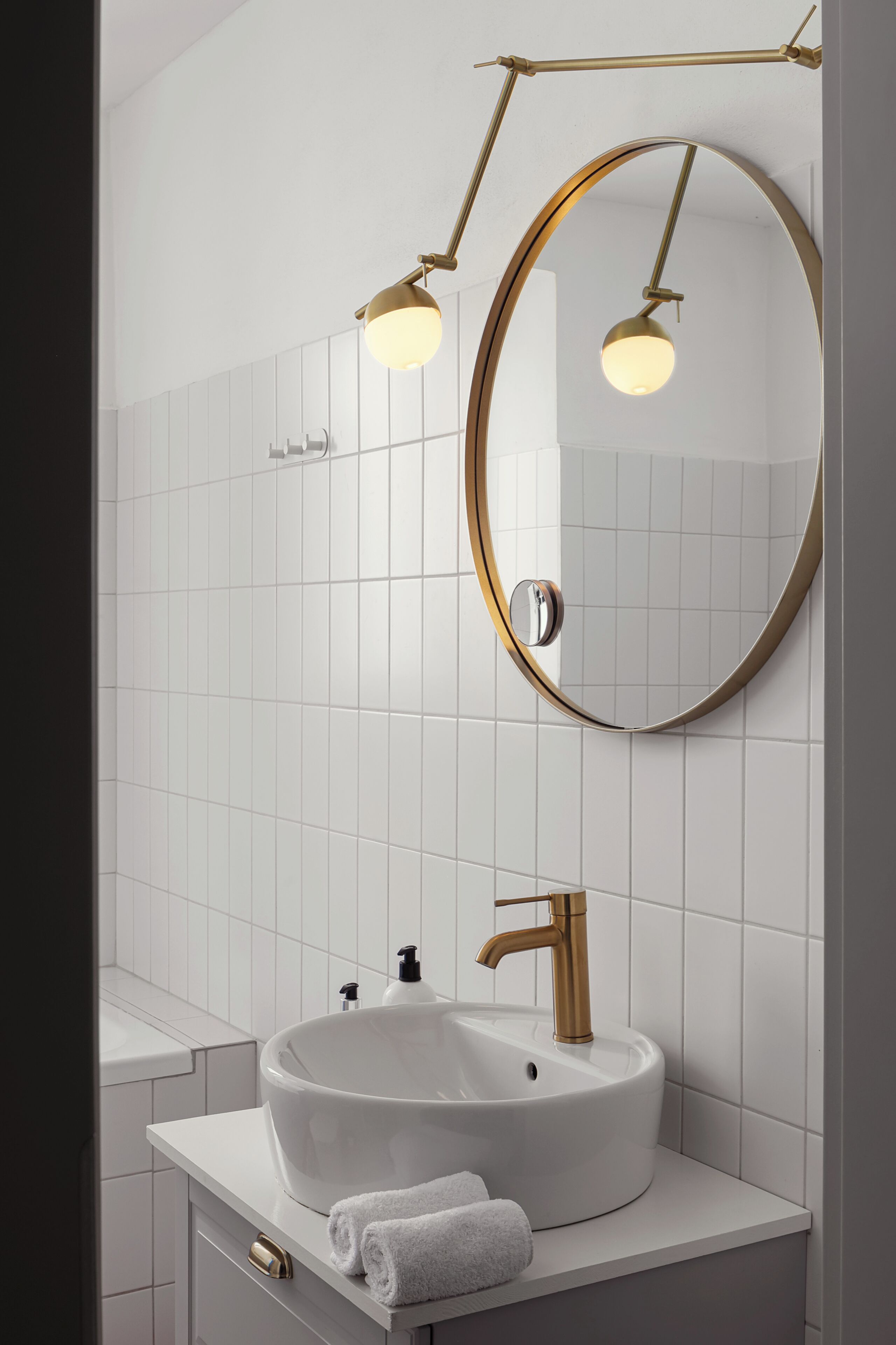 Un baño con lavamanos blanco, grifo dorado y un espejo redondo con marco dorado.